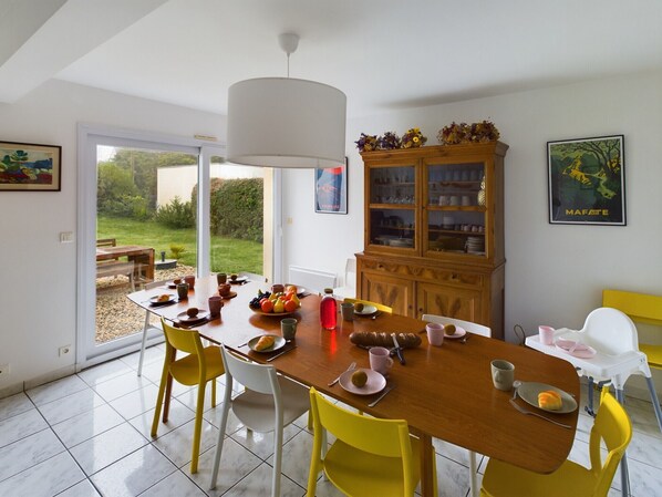 Un comedor con una mesa preparada para cuatro, sillas amarillas, un mueble de madera con puertas de vidrio y vistas a un jardín exterior a través de un ventanal.