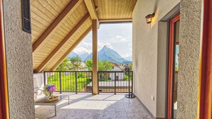A covered balcony with a view of mountains, a table with a vase of flowers, and a chair.