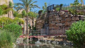 Un puente de piedra sobre una pequeña masa de agua, rodeado de exuberante vegetación y palmeras.