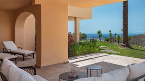 Un patio con mobiliario exterior, vista al océano y una palmera.