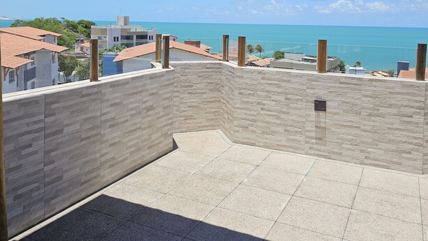A rooftop terrace with a view of the sea, featuring a tiled floor and a stone wall. - Comfort & Beautiful View 300m from Paradise - Wi-Fi/AC (Parnamirim)