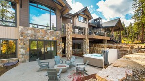 Una casa moderna de dos pisos con fachada de piedra, ventanas amplias y un patio con mobiliario exterior.