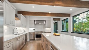Una cocina moderna con suelo de madera, electrodomésticos de acero inoxidable y grandes ventanales con vistas a zonas verdes.
