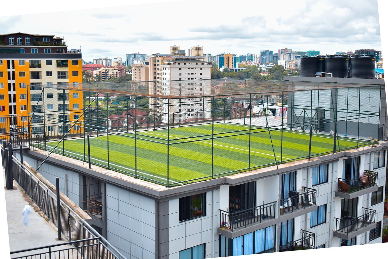 A modern building with a rooftop sports field, surrounded by other high-rise buildings.