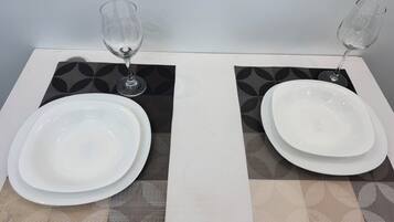 Una mesa dispuesta con dos platos blancos, una copa de vino y un vaso de agua sobre un mantel a cuadros.