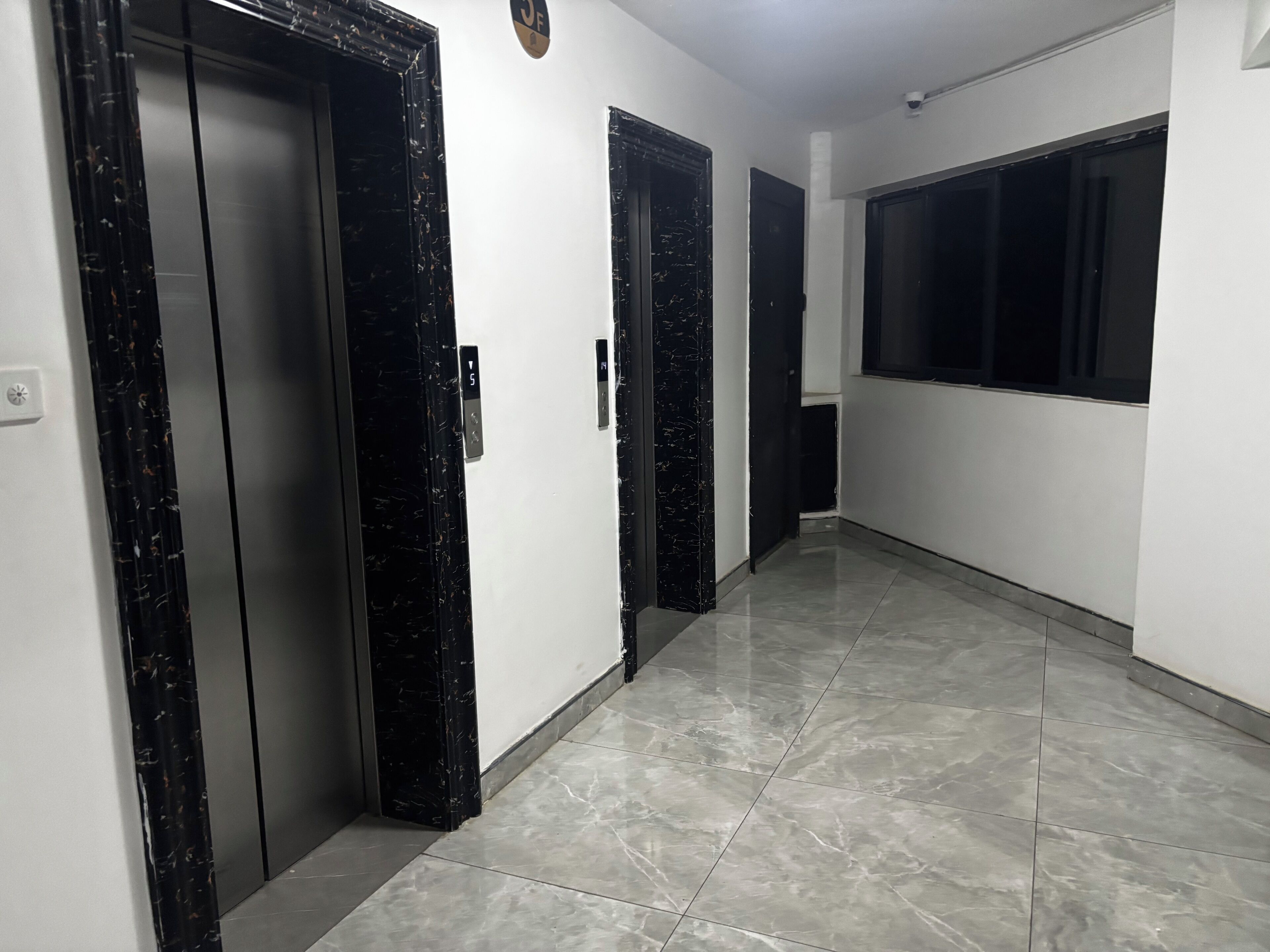 Un pasillo con puertas de marco negro, suelo de baldosas y una ventana a la derecha.