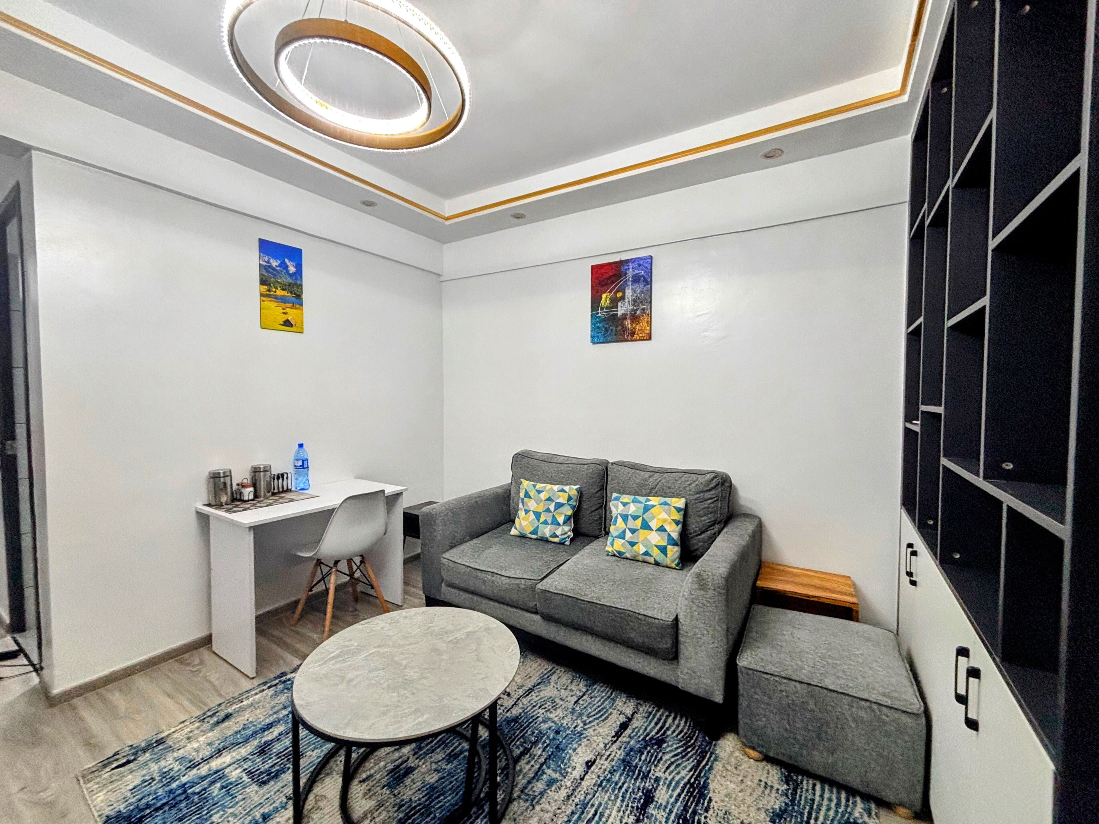 A modern room with a grey sofa, a small round table, a white desk, and a blue patterned rug.