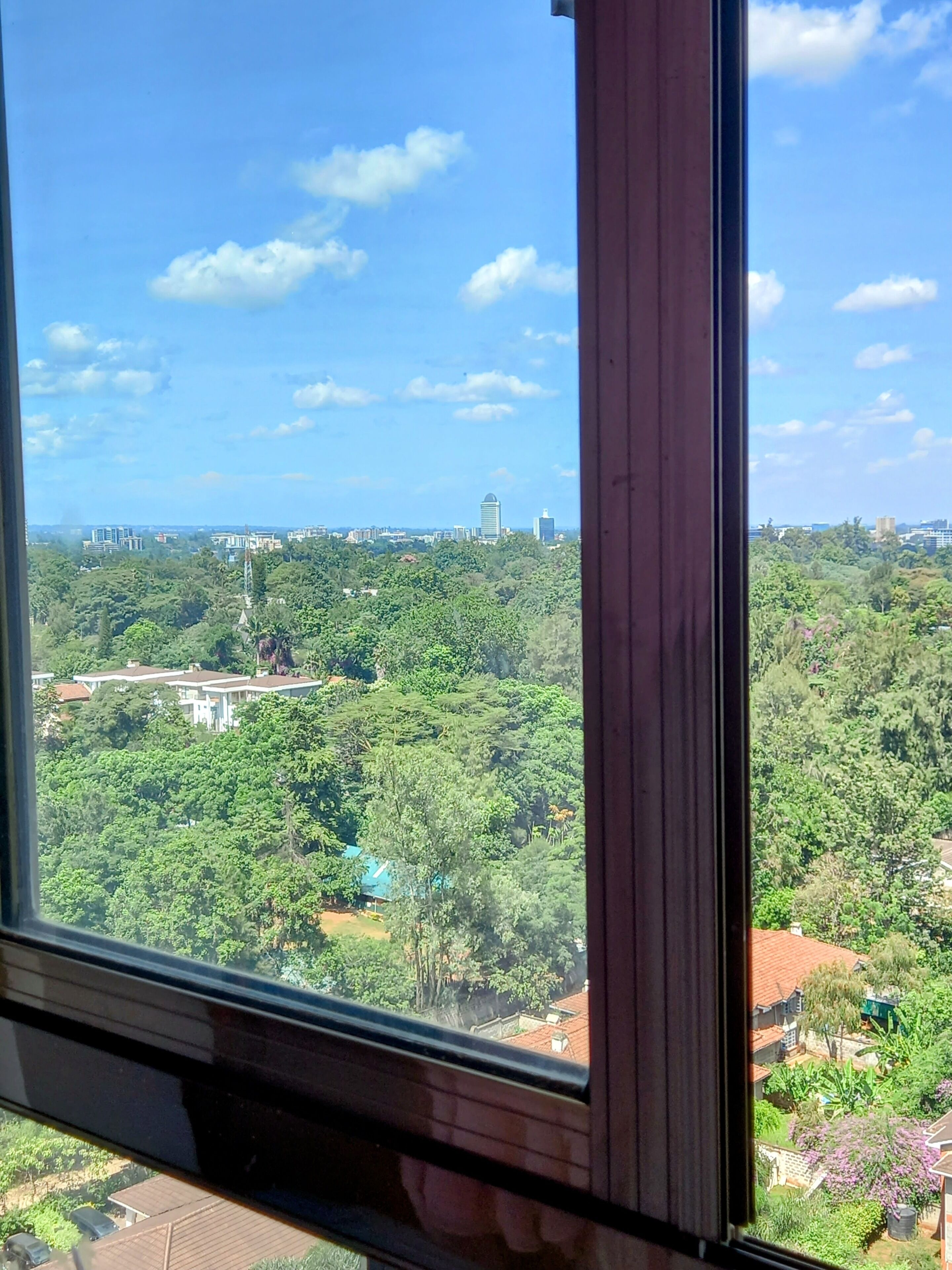 A view from a window overlooking a cityscape with buildings and greenery.