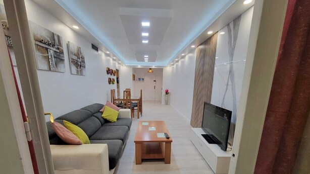 A modern living room with a sofa, coffee table, TV, and dining area. - SALOU FAMILY APARTMENT (Salou)
