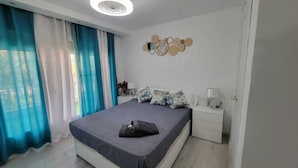A modern bedroom with a large bed, a bedside table, a lamp, and a decorative wall piece. - SALOU FAMILY APARTMENT (Salou)