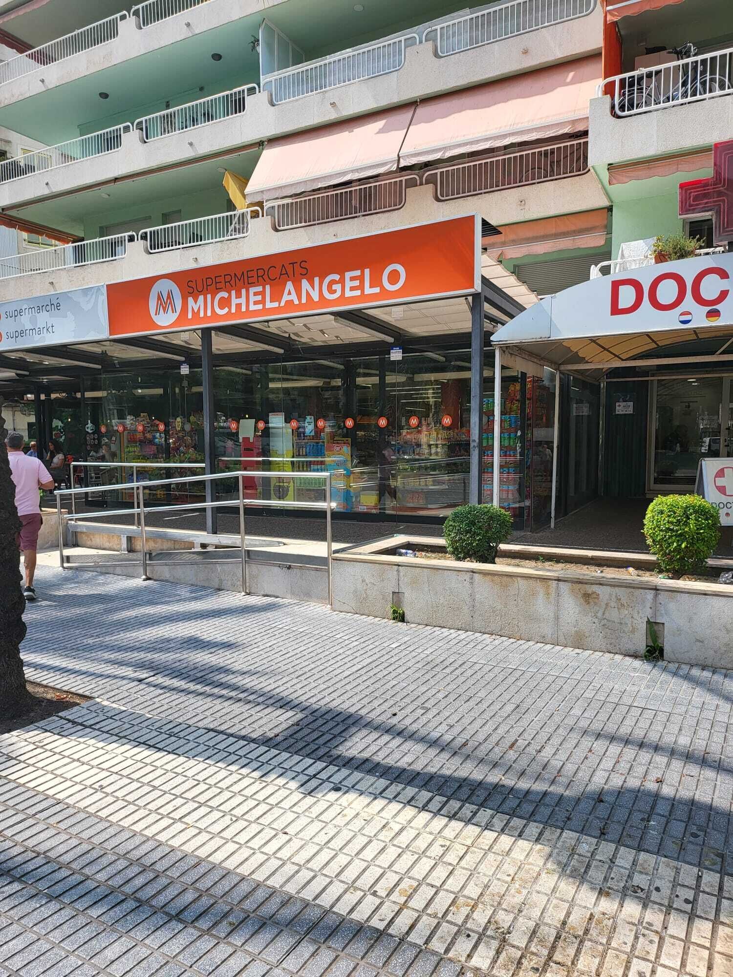 Eine Fußgängerzone mit einem Supermarkt namens 'MICHELANGEO' und einer Apotheke namens 'DOC'.