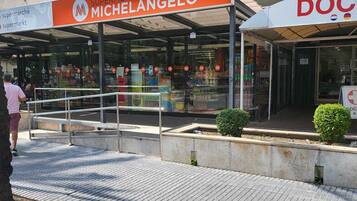 Eine Fußgängerzone mit einem Supermarkt namens 'MICHELANGEO' und einer Apotheke namens 'DOC'.