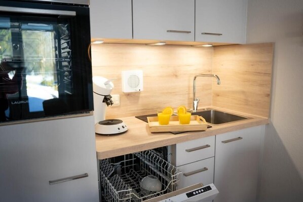 A compact kitchen with a built-in oven, a sink, and a dish drying rack.