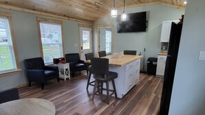 A spacious room with a wooden ceiling, a dining area with a table and chairs, a kitchen with a refrigerator and cabinets, and a television mounted on the wall. - Charming 2-bedroom, 2 full baths and pet friendly house near Mammoth Cave NP. (Mammoth Cave)