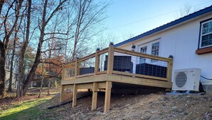 A wooden deck with a metal railing, a white building with a blue roof, and an air conditioning unit. - Charming 2-bedroom, 2 full baths and pet friendly house near Mammoth Cave NP. (Mammoth Cave)