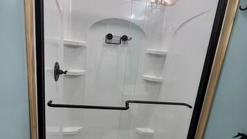 A shower enclosure with a glass door, a toilet, and a blue bath mat.