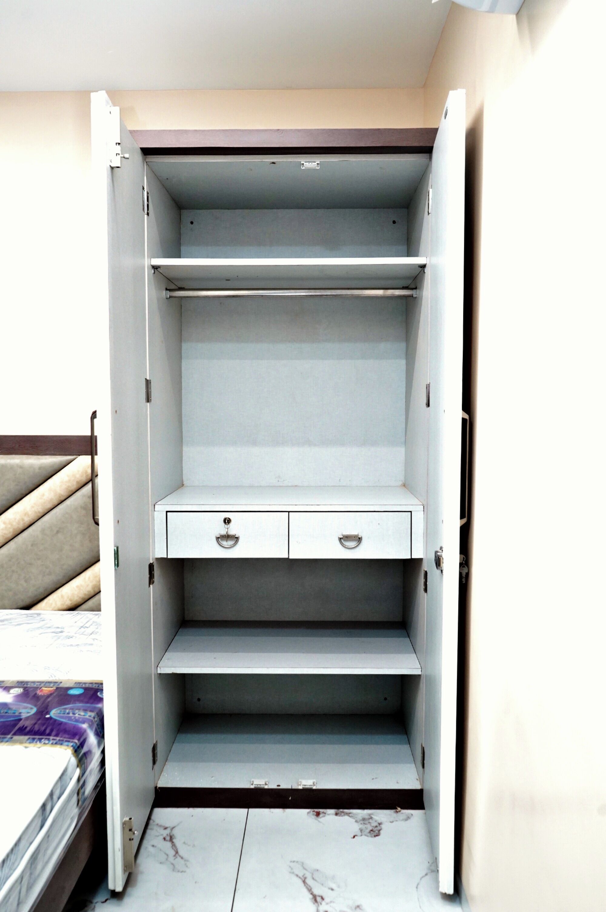 A wardrobe with two drawers and a shelf, a bed with a headboard, and a marble floor.