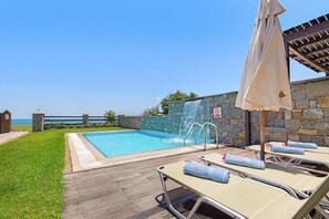 Ein Schwimmbecken mit Steinmauer, Liegestühlen und Sonnenschirm.