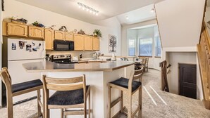 A modern kitchen with wooden cabinets, a central island with bar stools, a microwave, and a refrigerator. - Village Point #212: Private Hot Tub and Easy Access to Town and Slopes (Breckenridge)