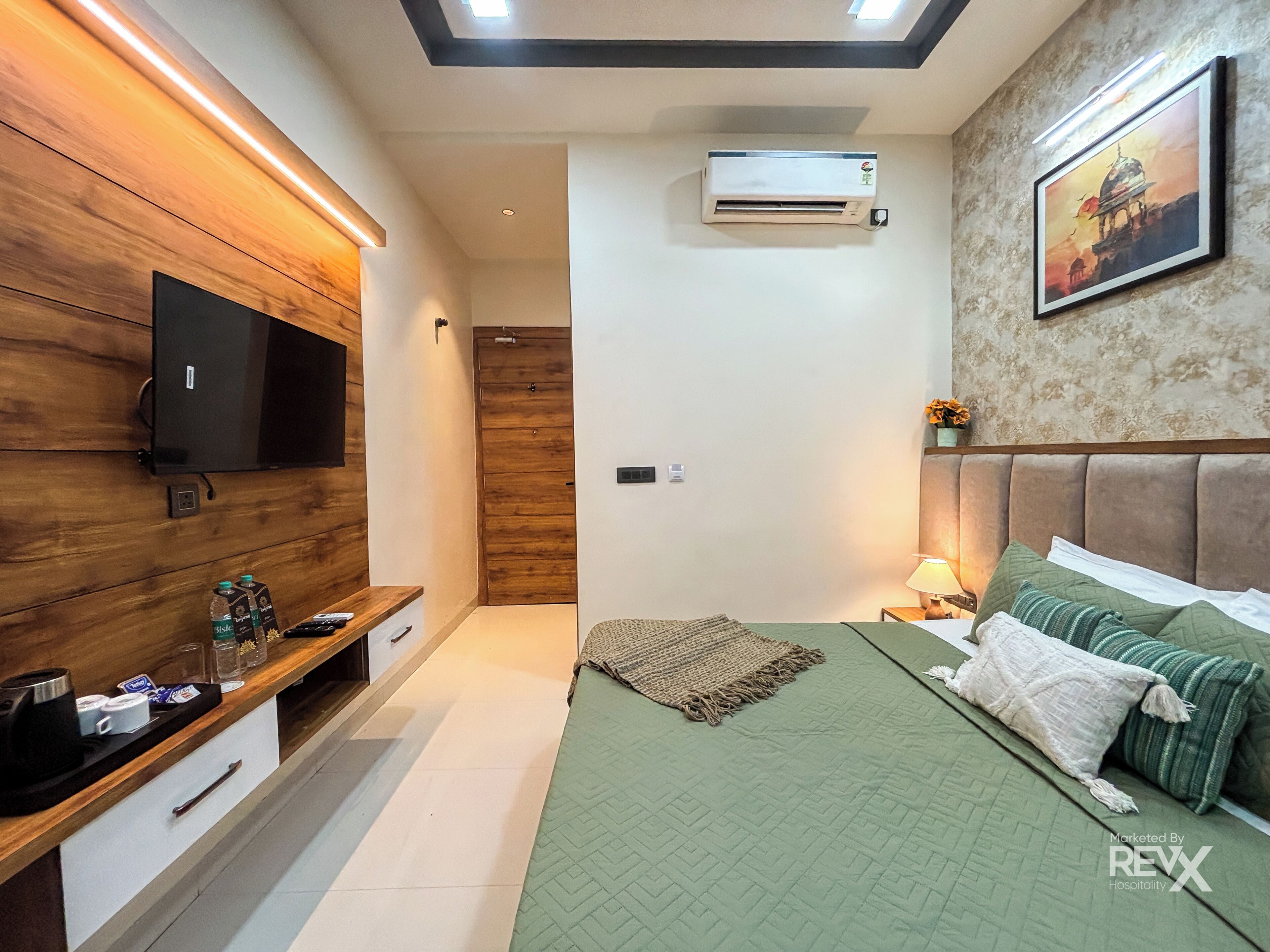 Una camera da letto moderna con televisione, aria condizionata, un letto con biancheria verde, un comodino e un quadro appeso al muro.