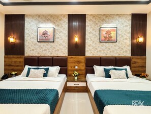 A hotel room with two beds, wooden headboards, floral wallpaper, and wall-mounted lights. - Hotel Brij Vas (Mathura)