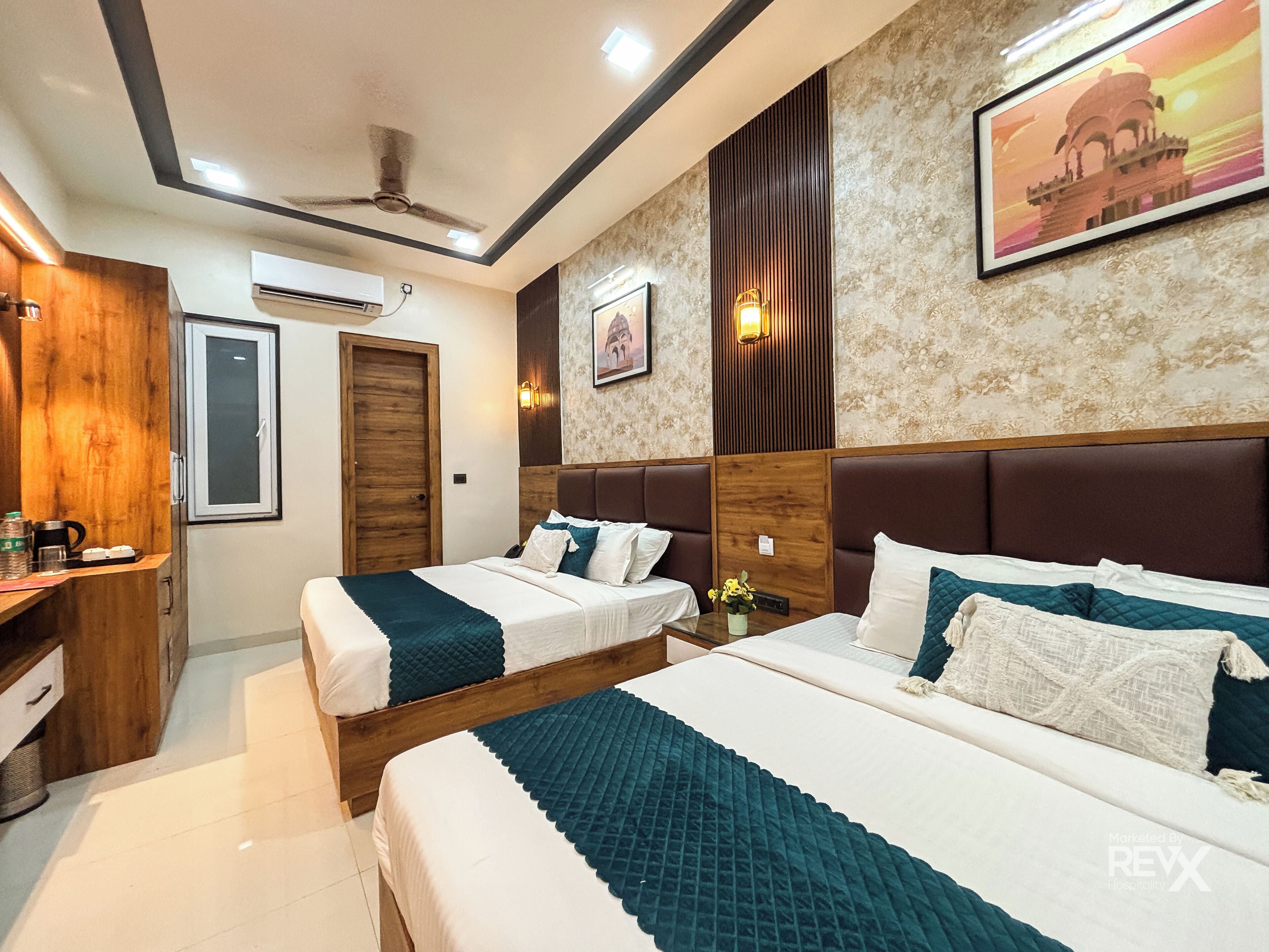 A hotel room with two beds, a wooden wardrobe, an air conditioning unit, and a framed picture on the wall.