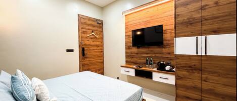 A modern bedroom with a bed, wooden wardrobe, TV, and a coffee machine.