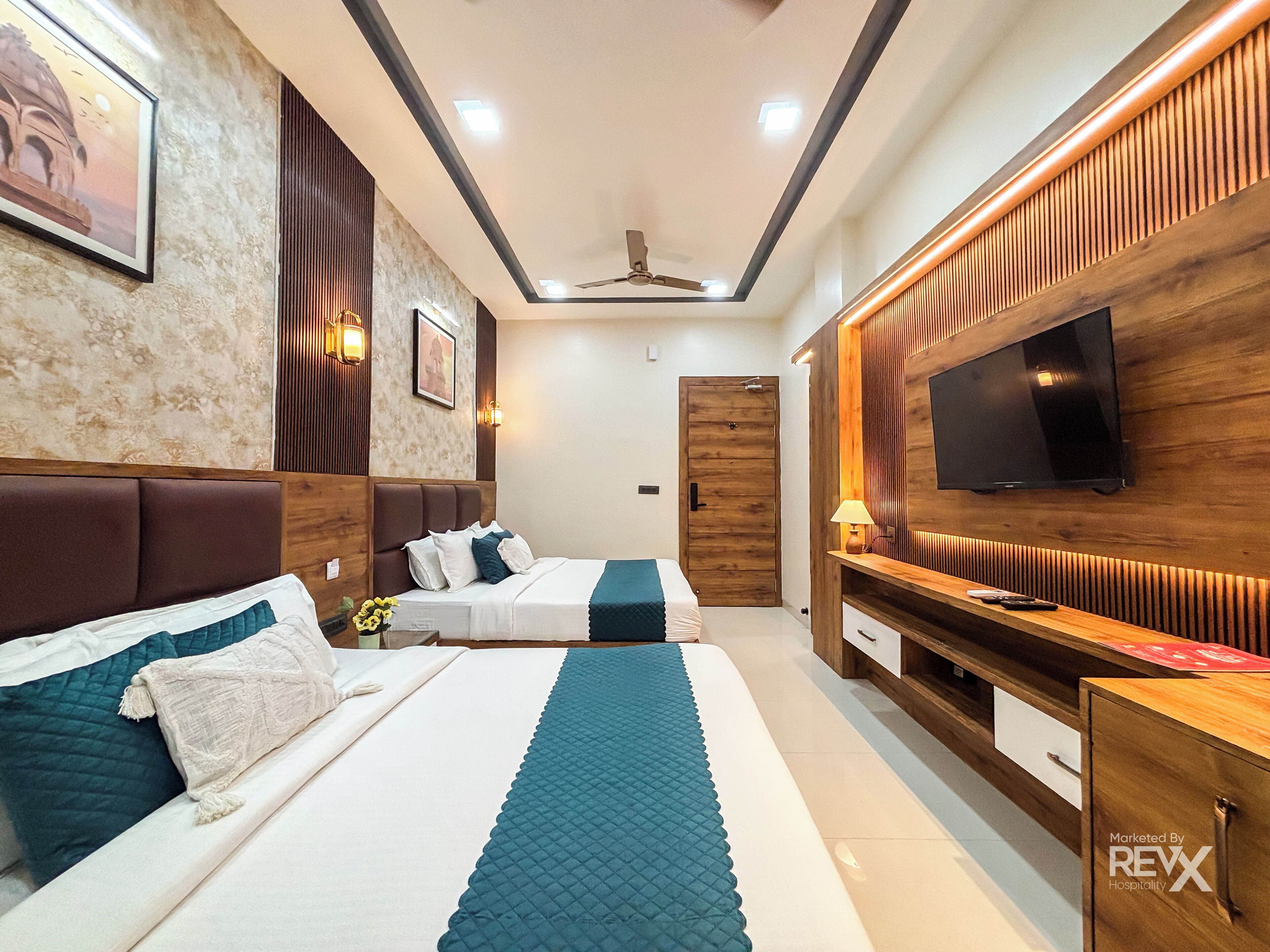A hotel room with two beds, a TV, a ceiling fan, and a wooden panel wall.