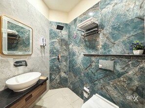 A bathroom with a marble wall, a sink, a mirror, a towel rack, and a potted plant. - Hotel Brij Vas (Mathura)