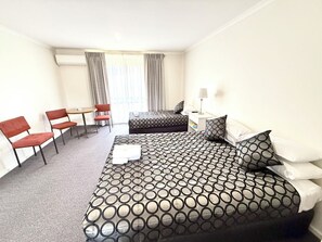 A hotel room with a bed, a desk, two chairs, a small table, and a lamp.