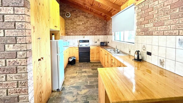 A kitchen with wooden cabinets, a brick wall, a tiled backsplash, a wooden countertop, and a black oven. - Redgum Motel (Mathoura)