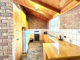 Cozinha com armários de madeira, parede de tijolos, painel de azulejos, bancada de madeira e forno preto.