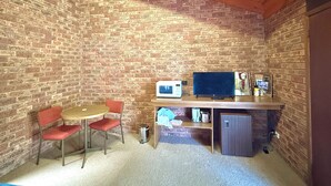 A small room with a brick wall, a wooden ceiling, a round table with two red chairs, a television, and a small refrigerator. - Redgum Motel (Mathoura)