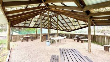 Un área de picnic techada con bancos y mesas de madera, rodeada por una valla de madera.