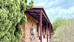 A covered outdoor area with brick walls and a metal roof, surrounded by dense greenery. - Redgum Motel (Mathoura)