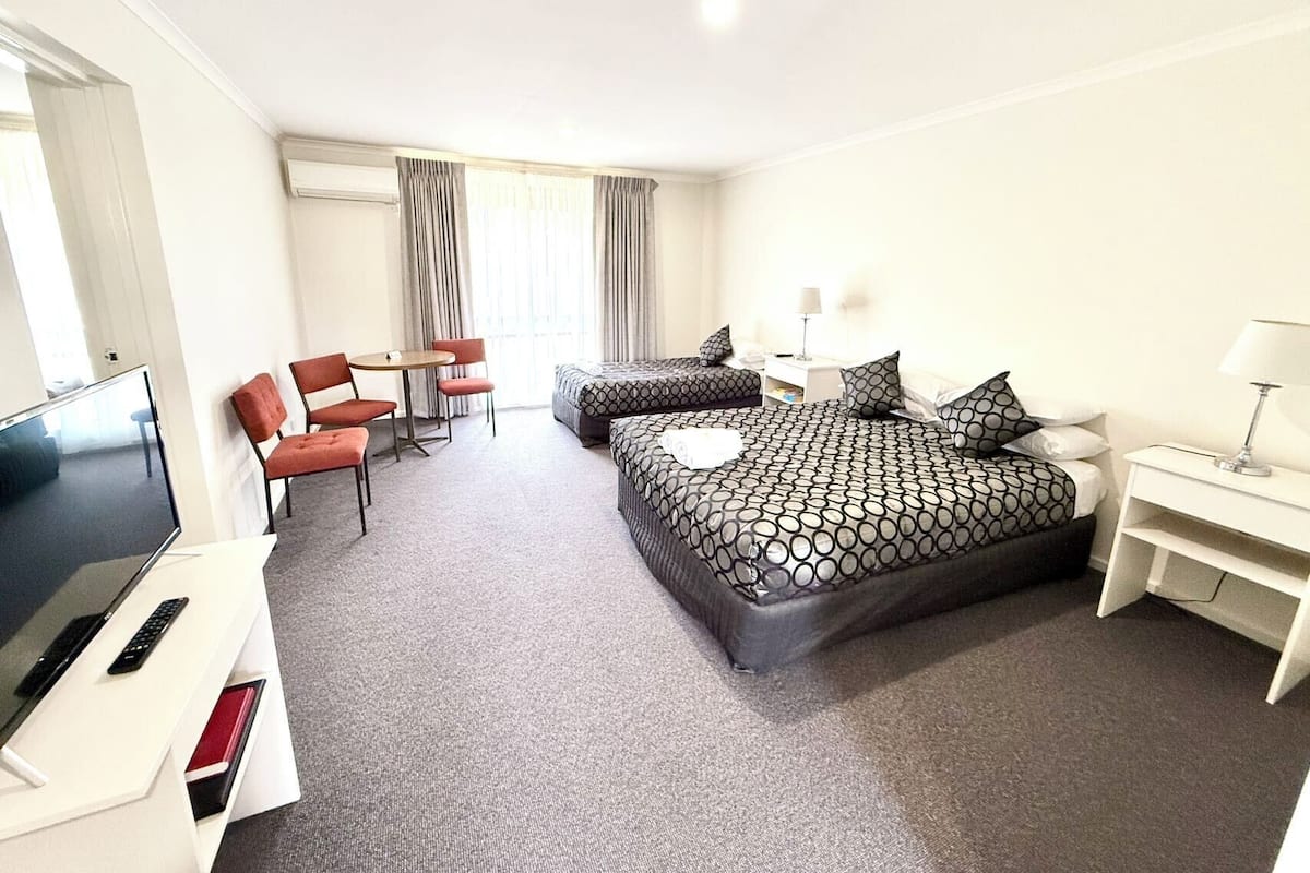 Una habitación de hotel con una cama, un escritorio con televisor, una silla y una ventana con cortinas.