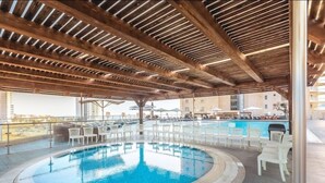Un área de piscina en la azotea con techo de madera, sillas de descanso y vista a edificios al fondo.