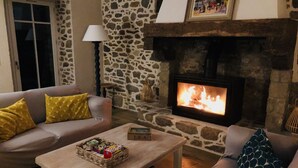 A cozy living room with a stone wall, a fireplace, and a sofa with yellow pillows. - At the heart of a market-garden farm on the Emerald Coast  (Saint-Lunaire)