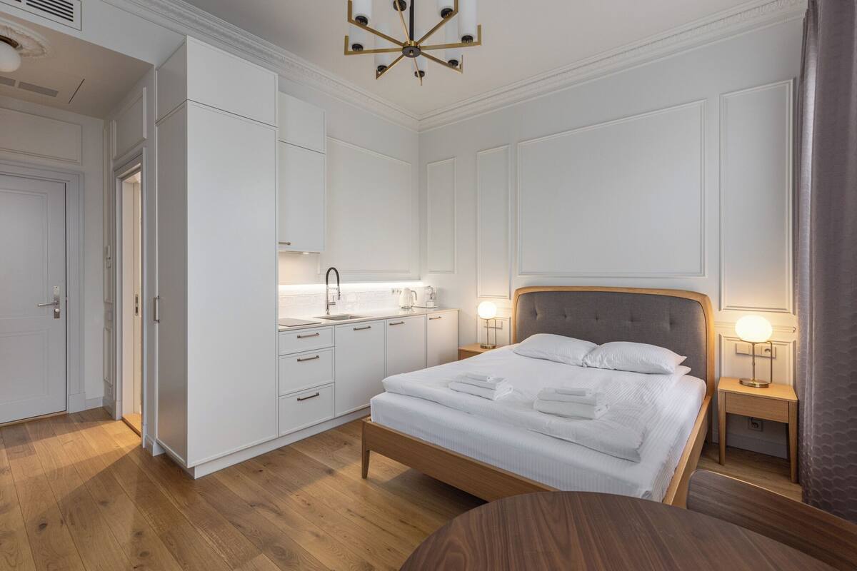 A bedroom with a bed, bedside tables, a nightstand, a wardrobe, and a kitchenette.