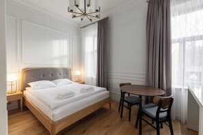 Camera d'albergo ordinata con un letto, lampade sui comodini, un tavolo con sedie e una vista attraverso tende leggere.