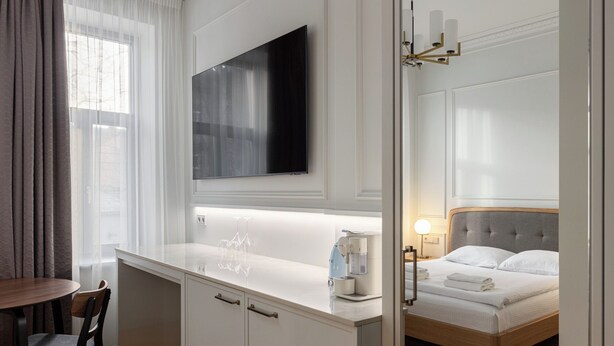 Una habitación de hotel moderna con una televisión de pantalla plana sobre una consola blanca, una cama con cabecera de madera y un pequeño comedor con una mesa redonda y dos sillas.