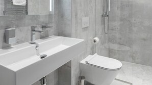 Un baño moderno con un espejo grande, un lavamanos blanco, un inodoro y una ducha.