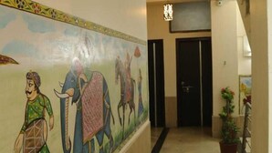 Un pasillo con un mural que representa a un hombre, un elefante y un caballo. Hay una puerta al final del pasillo y una planta en maceta a la derecha.