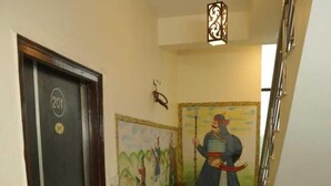Un pasillo con una puerta marcada '201', un mural de una figura histórica y plantas en macetas.