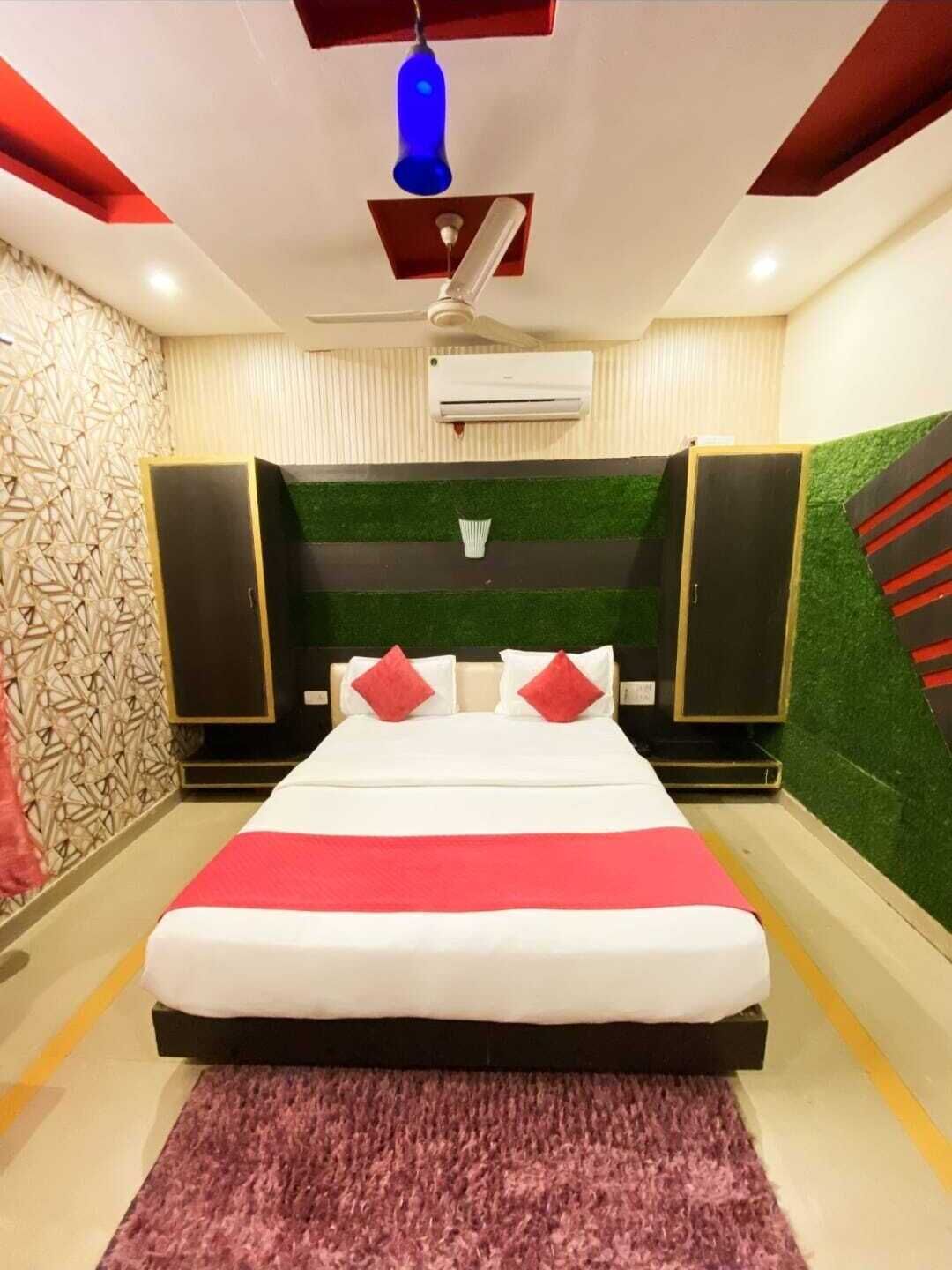 A modern hotel room with a large bed, a ceiling fan, an air conditioning unit, and a decorative wall with geometric patterns.