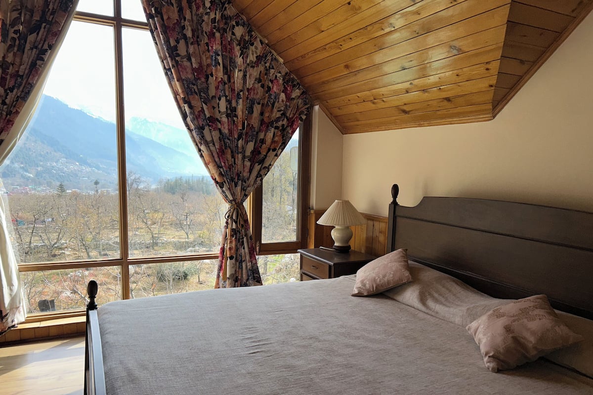 A bedroom with a large window, wooden ceiling, and a bed with pillows.