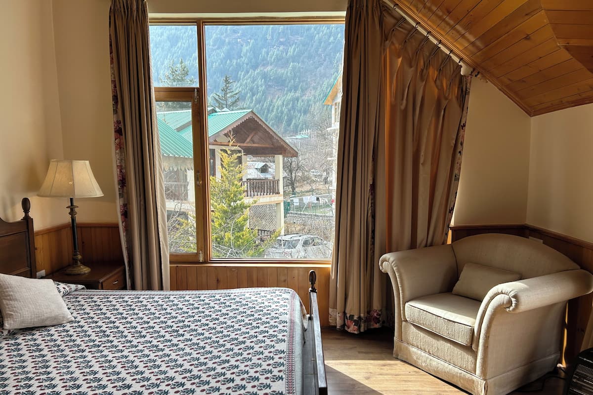 A bedroom with a bed, a chair, a lamp, and a window with curtains.