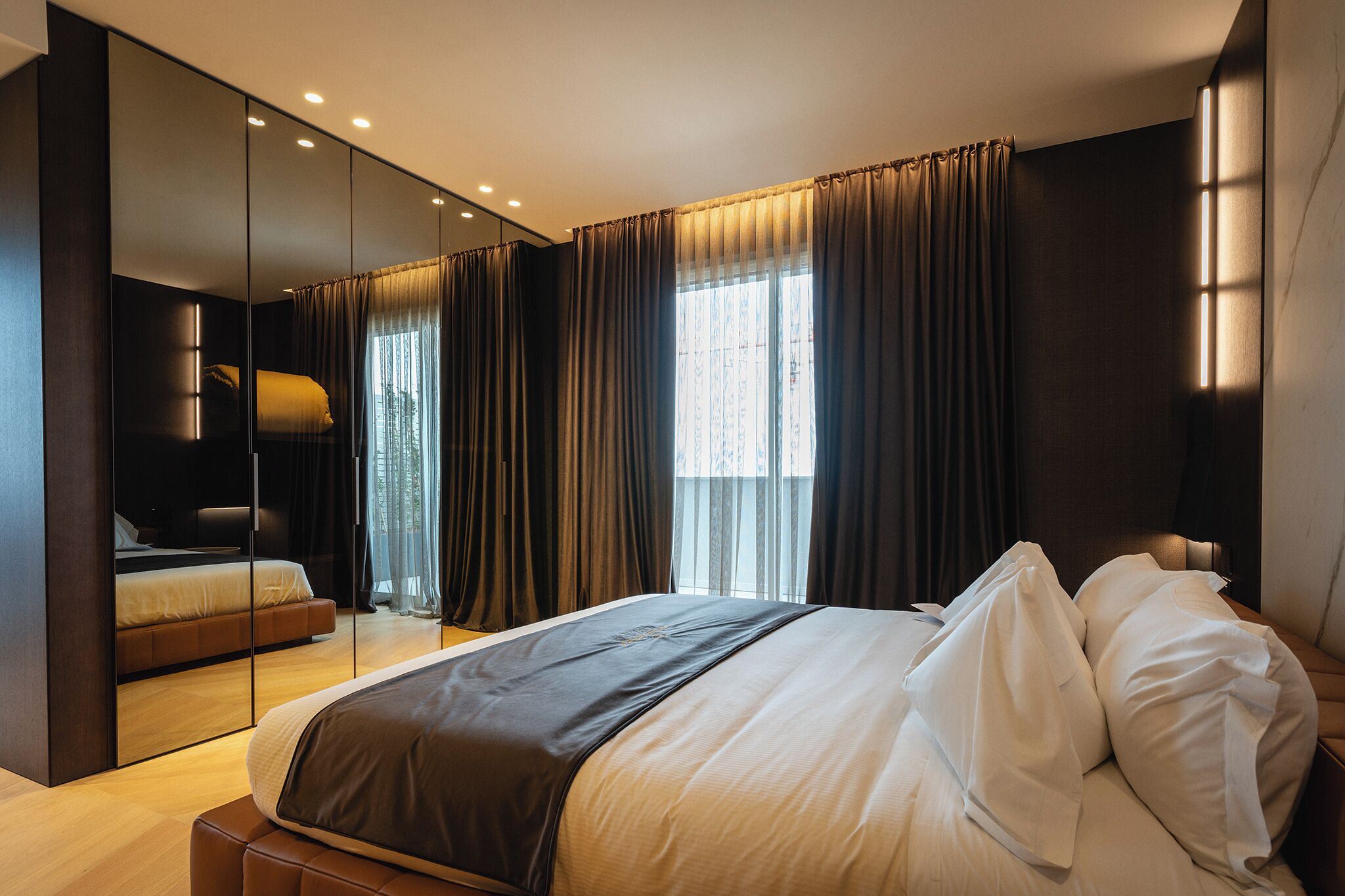 A modern hotel room with a large bed, a separate seating area, a large mirror, and a view of the outdoors.