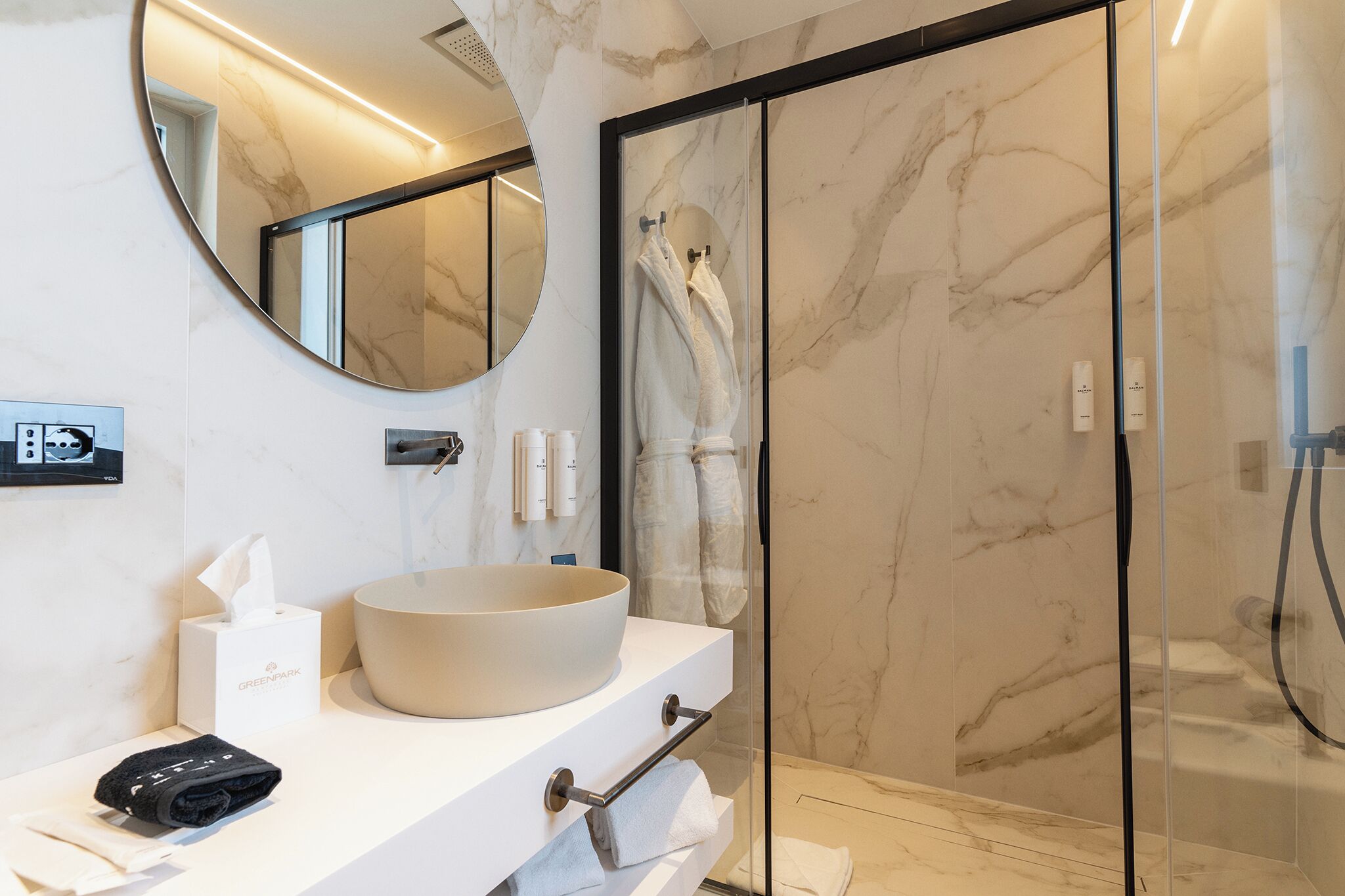 A modern bathroom with a large oval sink, a glass shower enclosure, and a marble wall.