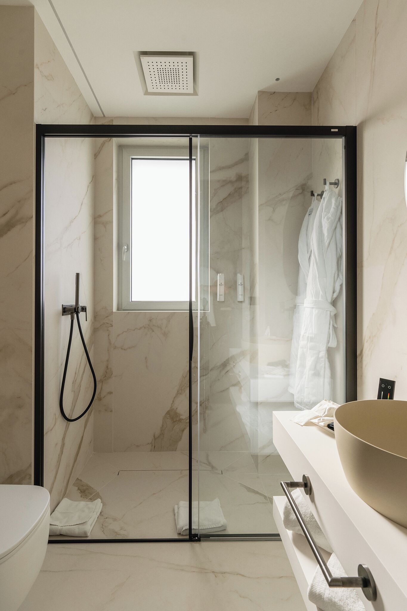 A modern bathroom with a glass shower enclosure, a white sink with a large bowl, and a towel rack.
